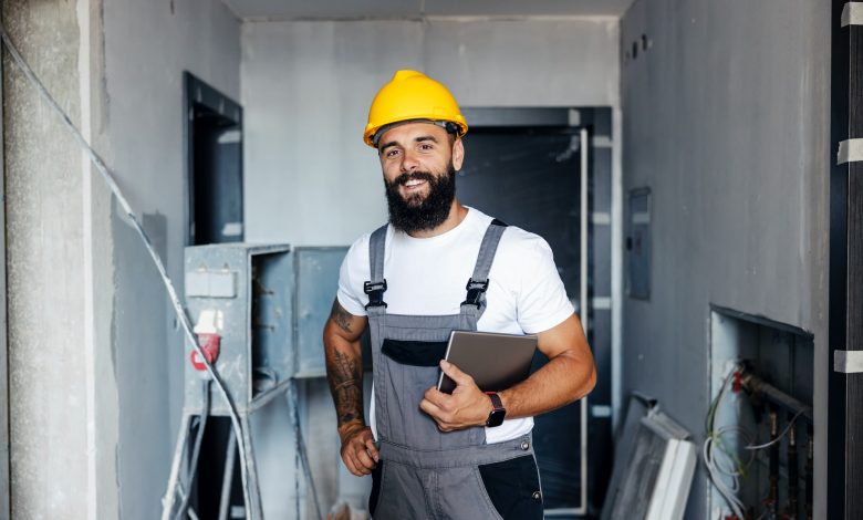 an electrician in a helmet and overalls is standing in the middle of a construction site