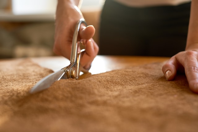 Female artisan cutting brown leather with scissors