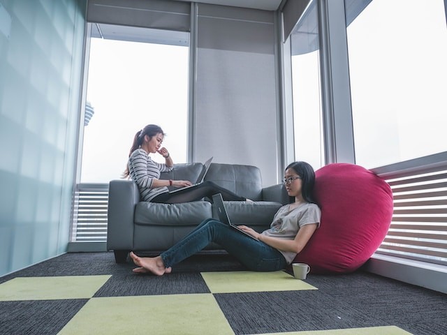 two women sitting on sofa and floor inside gray painted room