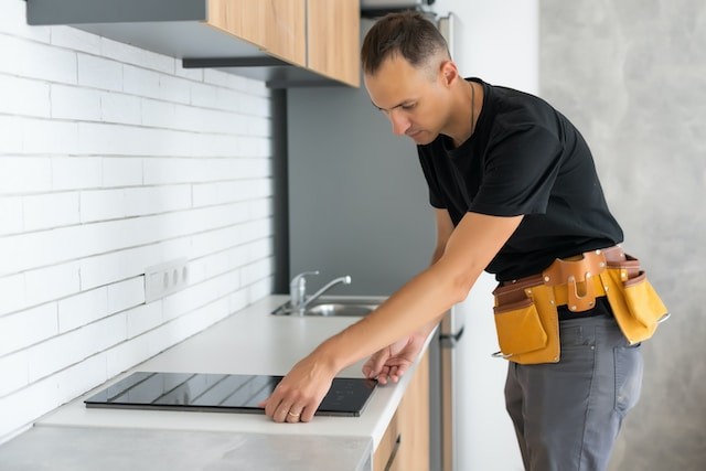 young repairman installing induction cooker in kitchen