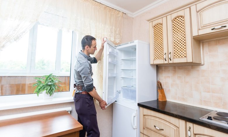 young male repairman fixing refrigerator in kitchen