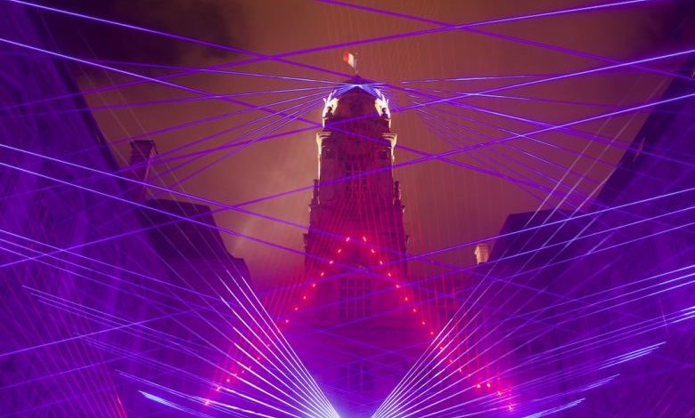 Laser Level - man in black jacket standing on blue and yellow string lights