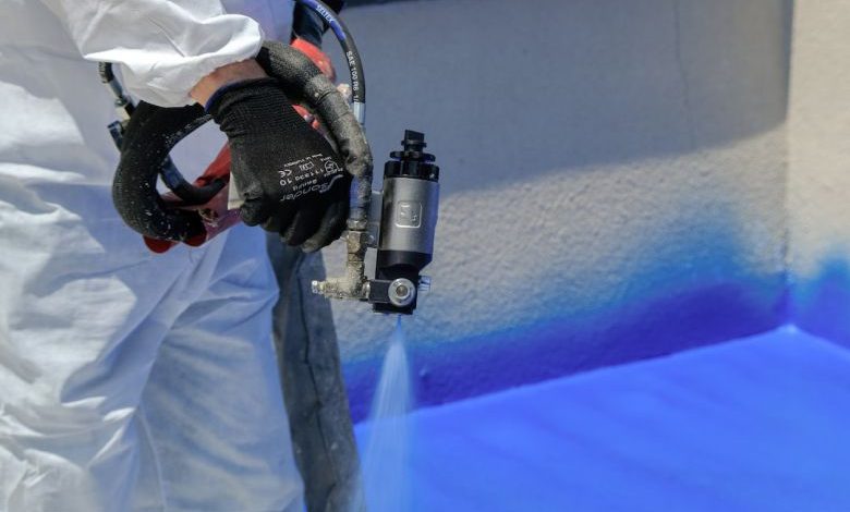 Spray Insulation - a man in white coveralls painting a wall with blue paint