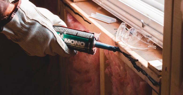 Caulking - Crop unrecognizable workman in glove applying caulk from bottle on seam during window montage work in building