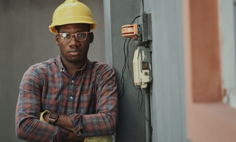 Electrician's Tools - man in blue white and red plaid button up shirt wearing yellow hard hat holding black