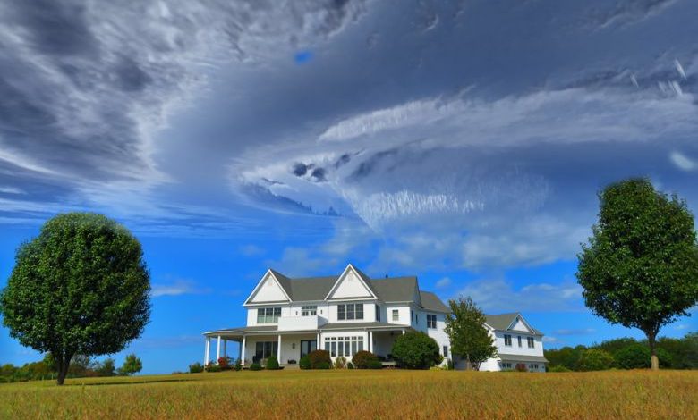 Building A Home - white and gray house between two green tall trees under gray clouds forming swirl during daytime