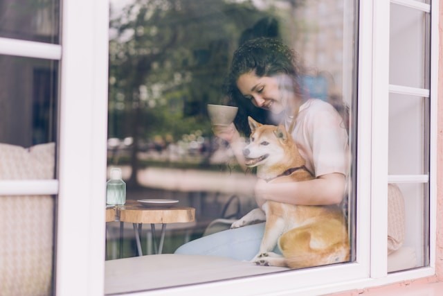 a-woman-sitting-on-a-window-sill-holding-a-dog