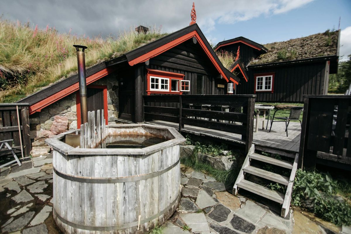 Charming rustic cabin exterior with a vintage wooden hot tub in a lush outdoor setting.