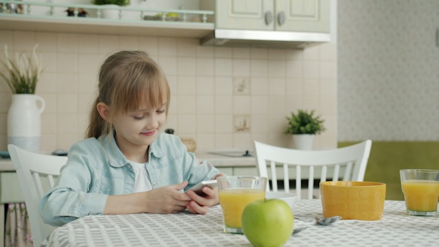 girl-using-smartphone-at-kitchen-table-with-breakfast